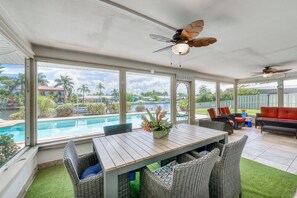 A covered patio with a pool view, wicker furniture, ceiling fans, and a sign reading "BEACH HOUSE".