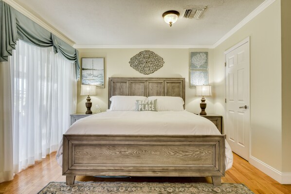A bedroom with a wooden bed, two bedside tables with lamps, a decorative wall piece, and a door.