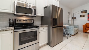 Una cocina moderna con electrodomésticos de acero inoxidable, armarios blancos y piso de baldosas.
