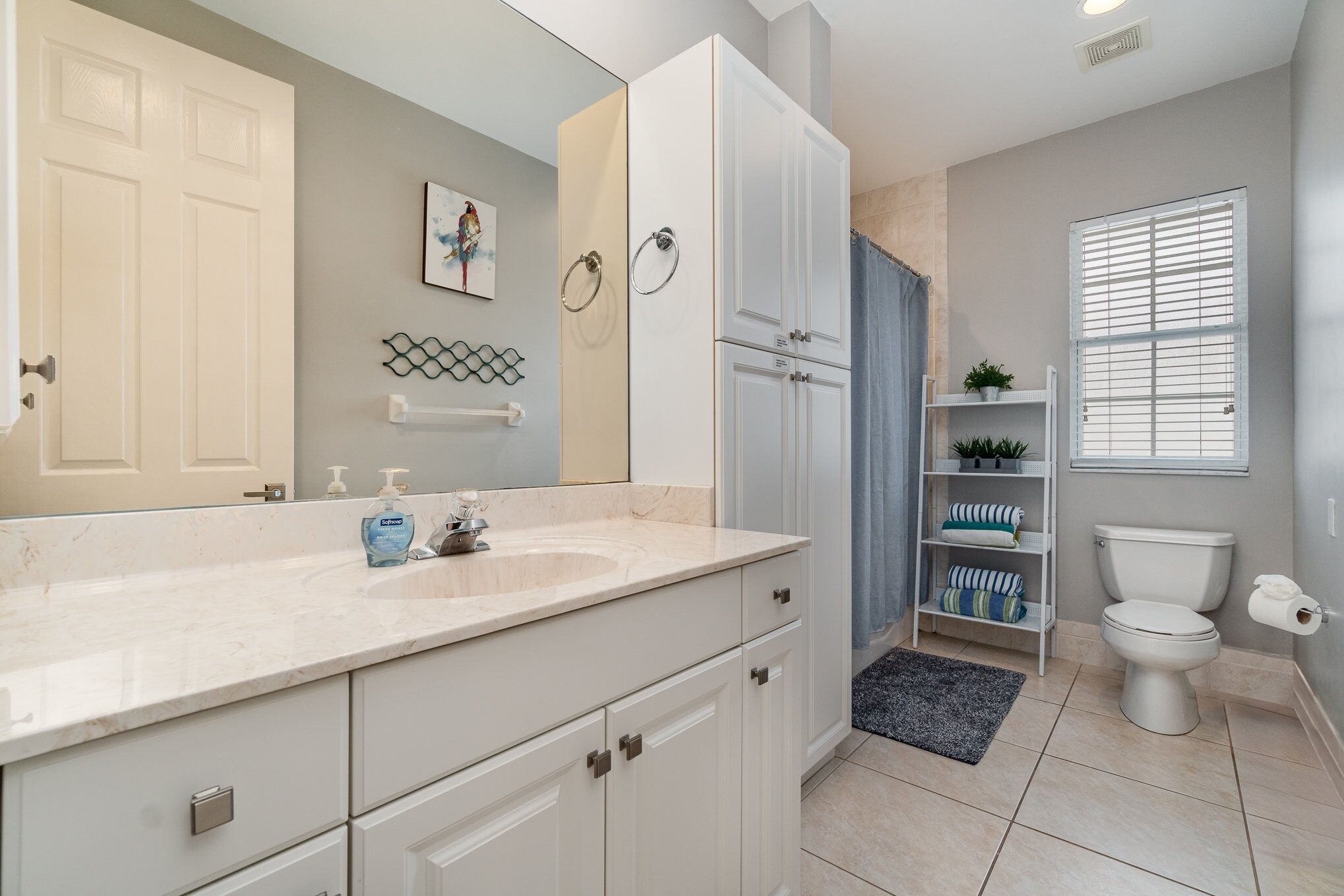Une salle de bain avec un meuble-lavabo blanc, un lavabo avec des distributeurs de savon, des toilettes, un rideau de douche et une étagère avec des serviettes.