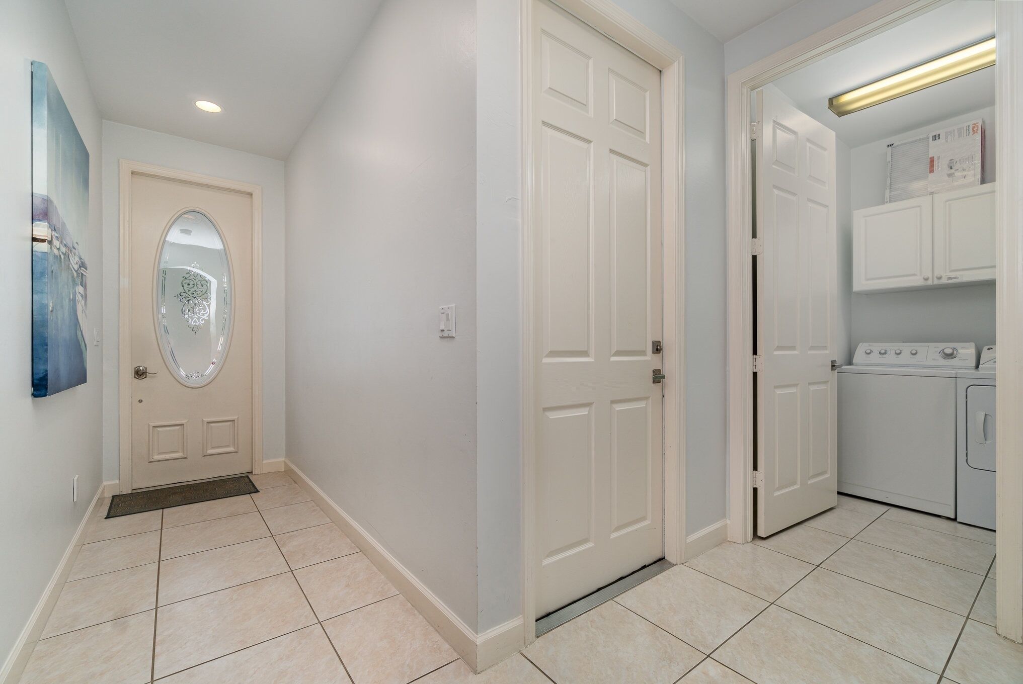A hallway with a white door, a doormat, and a laundry area with a washing machine.