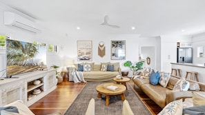 A spacious living room with a large TV, a fireplace, a sofa set, and a kitchen area.