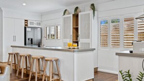 Una cocina moderna con muebles blancos, una isla central con taburetes, un refrigerador y una cafetera.