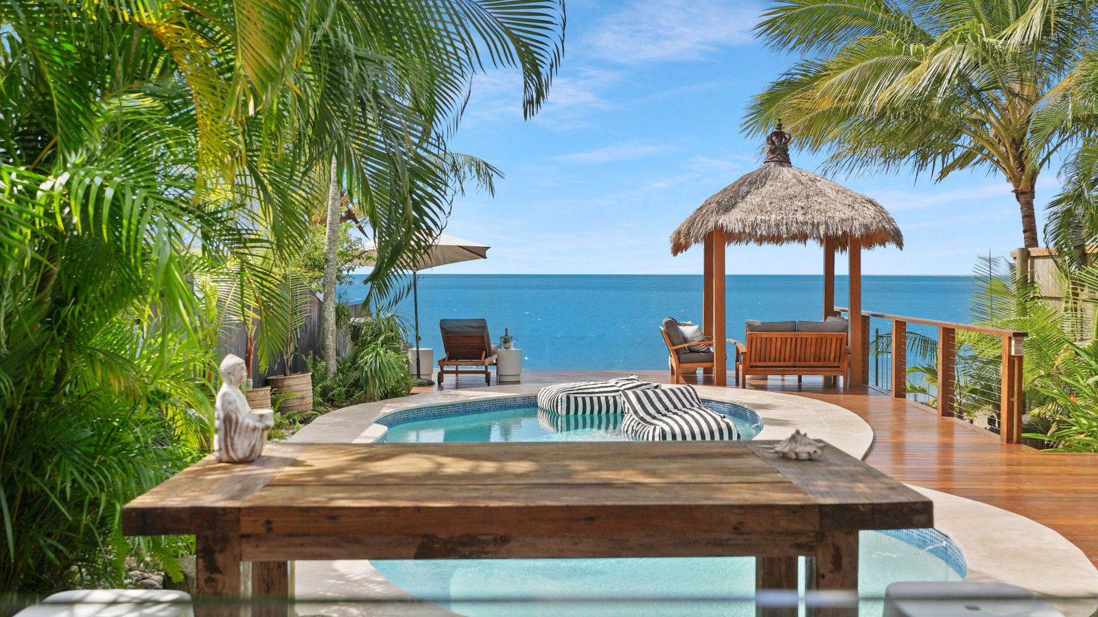 Un espace piscine avec des chaises longues et un gazebo à toit de chaume offrant une vue sur l’océan.