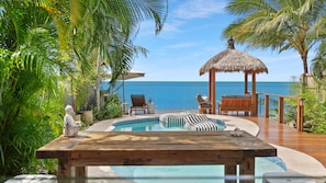 A pool area with lounge chairs and a thatched gazebo overlooking the ocean.