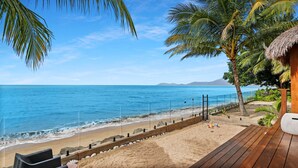 Blick auf einen Strand mit Holzterrasse, Palmen und blauem Himmel.