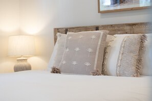 Een bed met drie kussens, een lamp en een lijst met een foto aan de muur.