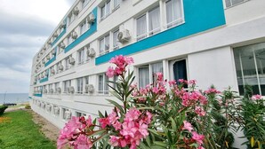 A multi-story hotel with air conditioning units on the exterior walls, a balcony on the second floor, and a view of the sea in the background. - Hotel Capitol Eforie Sud (Eforie)