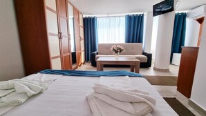 A hotel room with a bed, a sofa, a coffee table with a vase of flowers, and a TV mounted on the wall. - Hotel Capitol Eforie Sud (Eforie)