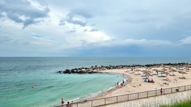 A beach with a rocky breakwater, sandy shore, and umbrellas. - Hotel Capitol Eforie Sud (Eforie)