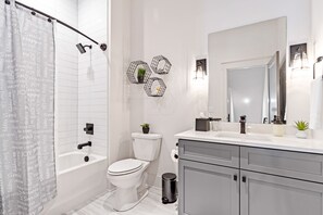 Um banheiro moderno com parede revestida de azulejos brancos, cortina de chuveiro com palavras positivas, vaso sanitário, pia com espelho e lixeira.