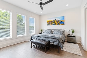 A bedroom with a bed, a bench, a nightstand, a ceiling fan, and a cityscape painting on the wall.