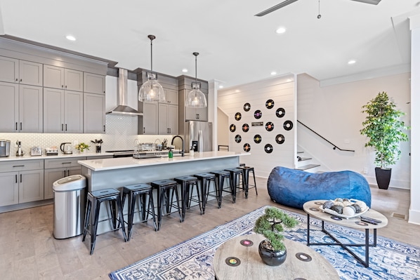 A modern kitchen with grey cabinets, a central island with bar stools, pendant lighting, and a wall decorated with vinyl records.