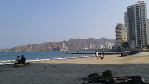 Una playa con montañas al fondo, algunas personas y un edificio grande.