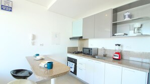 Una cocina compacta con armarios blancos, encimera de granito, microondas, licuadora roja y cafetera.