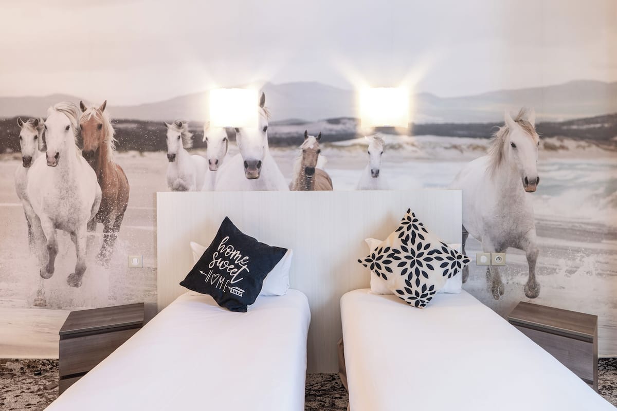 A hotel room with two beds, a large horse-themed mural on the wall, and a pillow with the text "home sweet home."