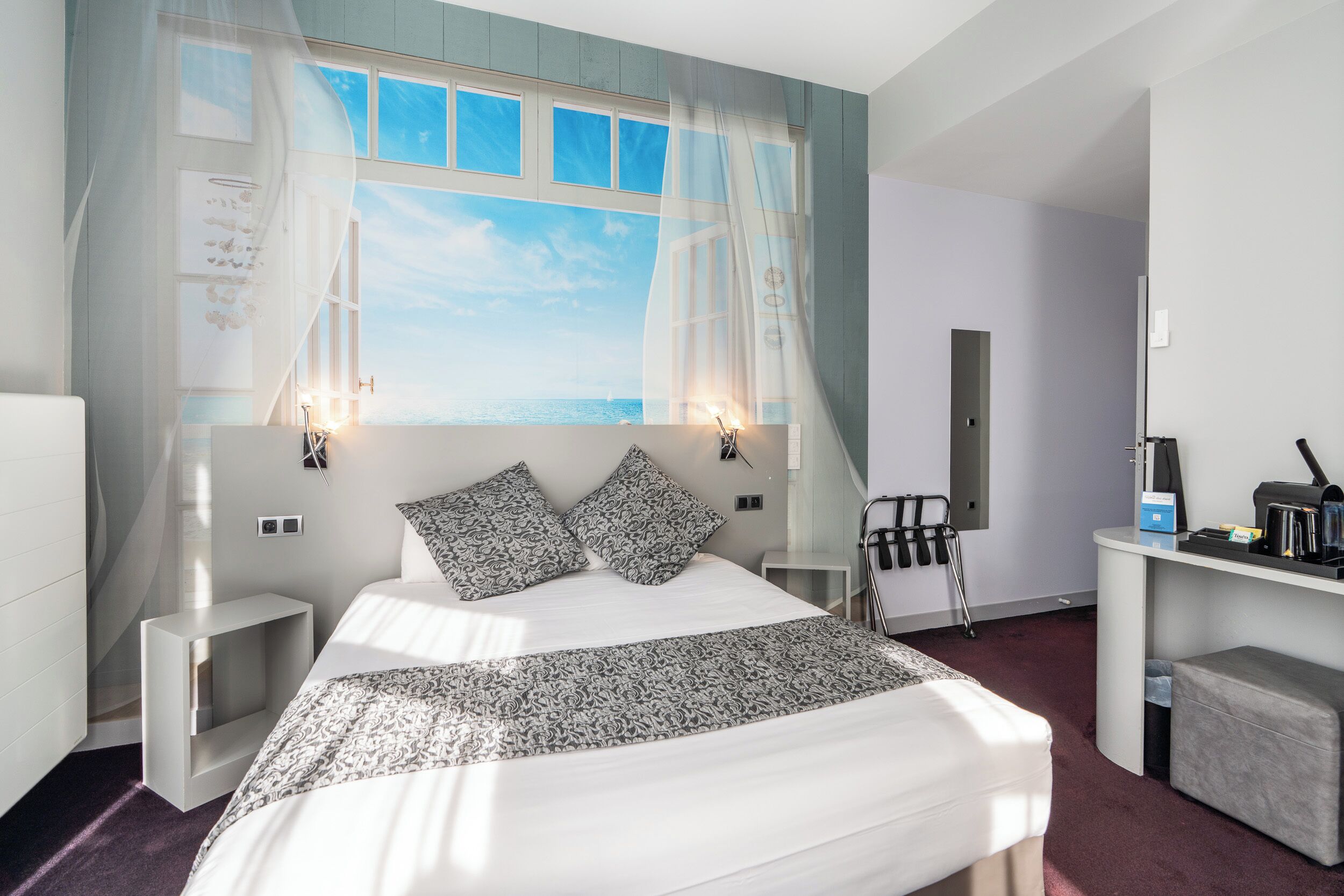Habitación de hotel moderna con una cama grande, un escritorio y vistas al mar a través de una ventana.