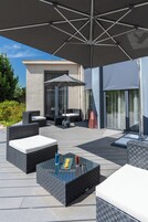 Uma área de estar ao ar livre com assentos, uma mesa e um grande guarda-sol.