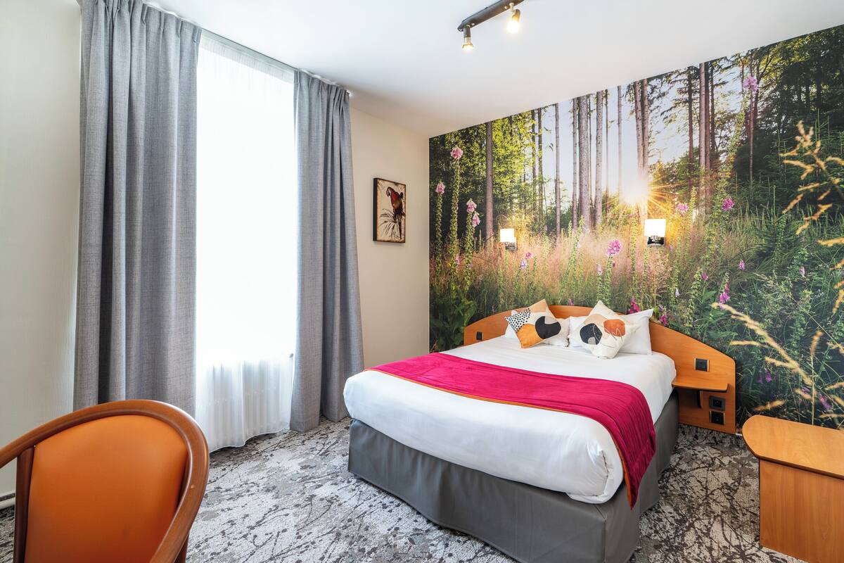 A hotel room with a large bed, a chair, a nightstand, and a forest-themed wall mural.