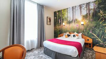 A hotel room with a large bed, a chair, a nightstand, and a forest-themed wall mural.