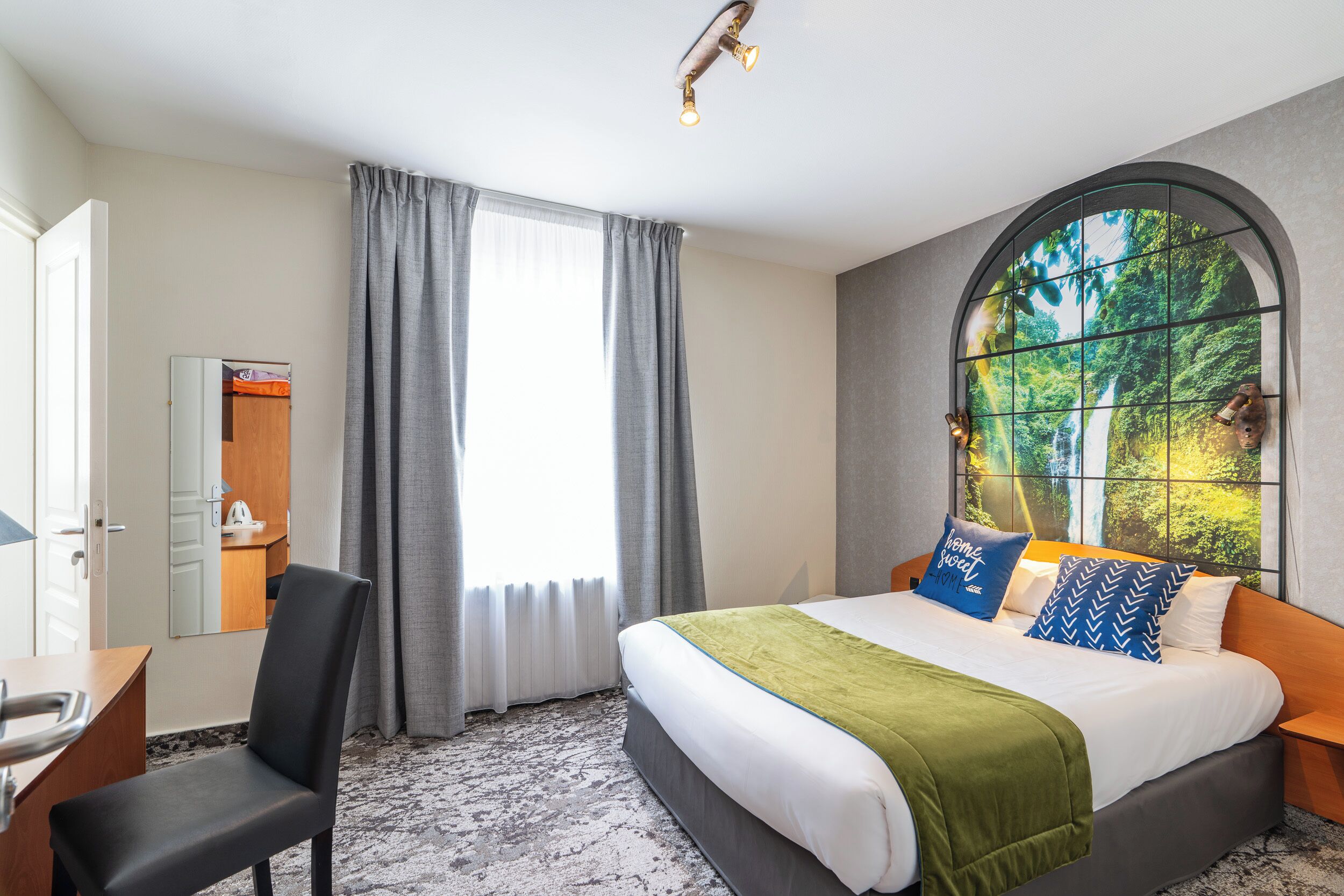 Habitación de hotel con cama, escritorio, silla, ventana con cortinas y vista a zonas verdes.
