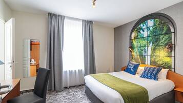 Camera d'albergo con un letto, una scrivania, una sedia, una finestra con tende e vista sul verde.