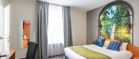 Habitación de hotel con cama, escritorio, silla, ventana con cortinas y vista a zonas verdes.