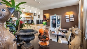 A dining area with a bar, seating, and decorative items including a fish sculpture, a vase with dried flowers, and a cat sculpture. - Logis Hotel des Ducs (Alencon)