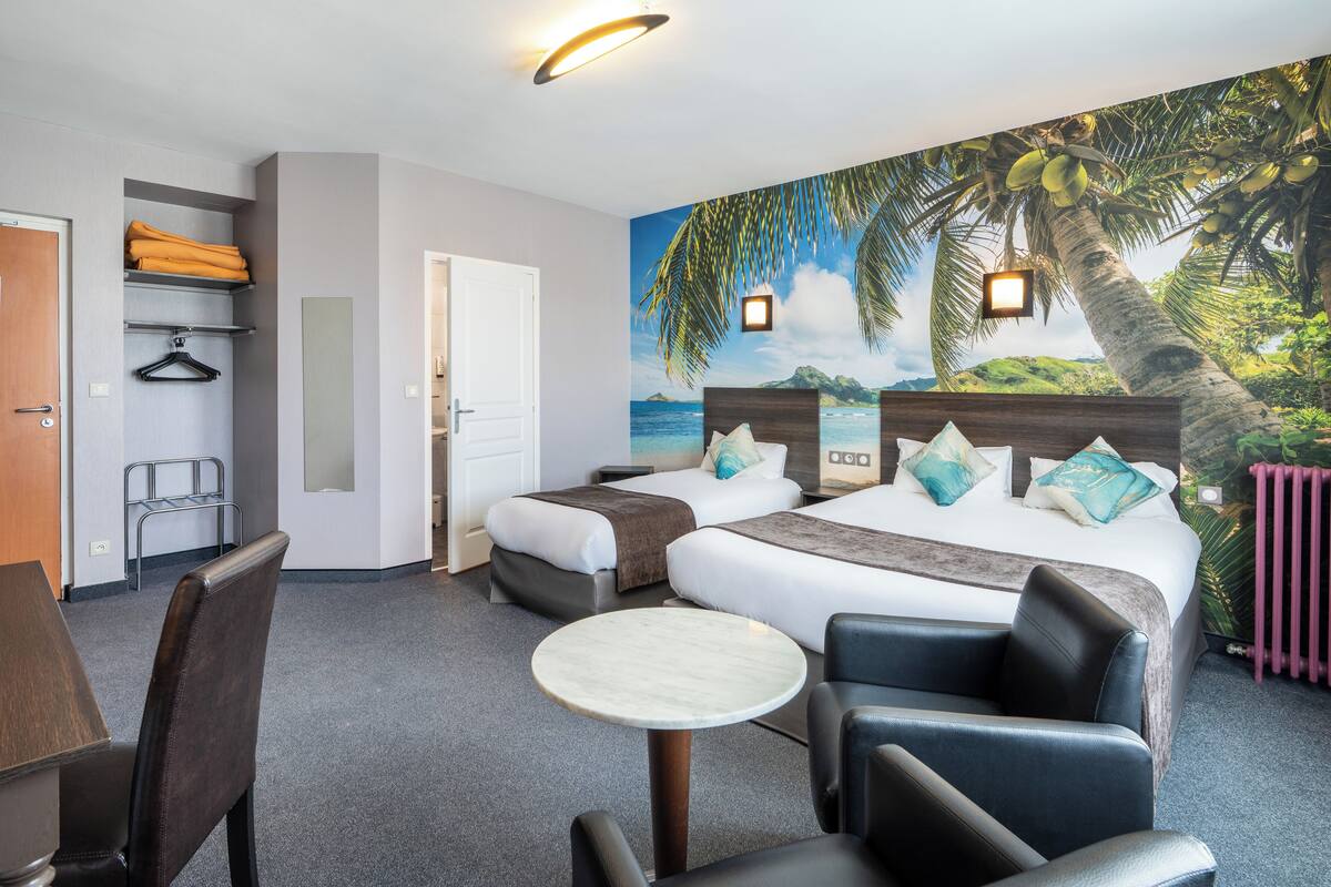A hotel room with two beds, a small table, chairs, a coat rack, and a mural of a tropical beach.