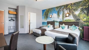 A hotel room with two beds, a small table, chairs, a coat rack, and a mural of a tropical beach.