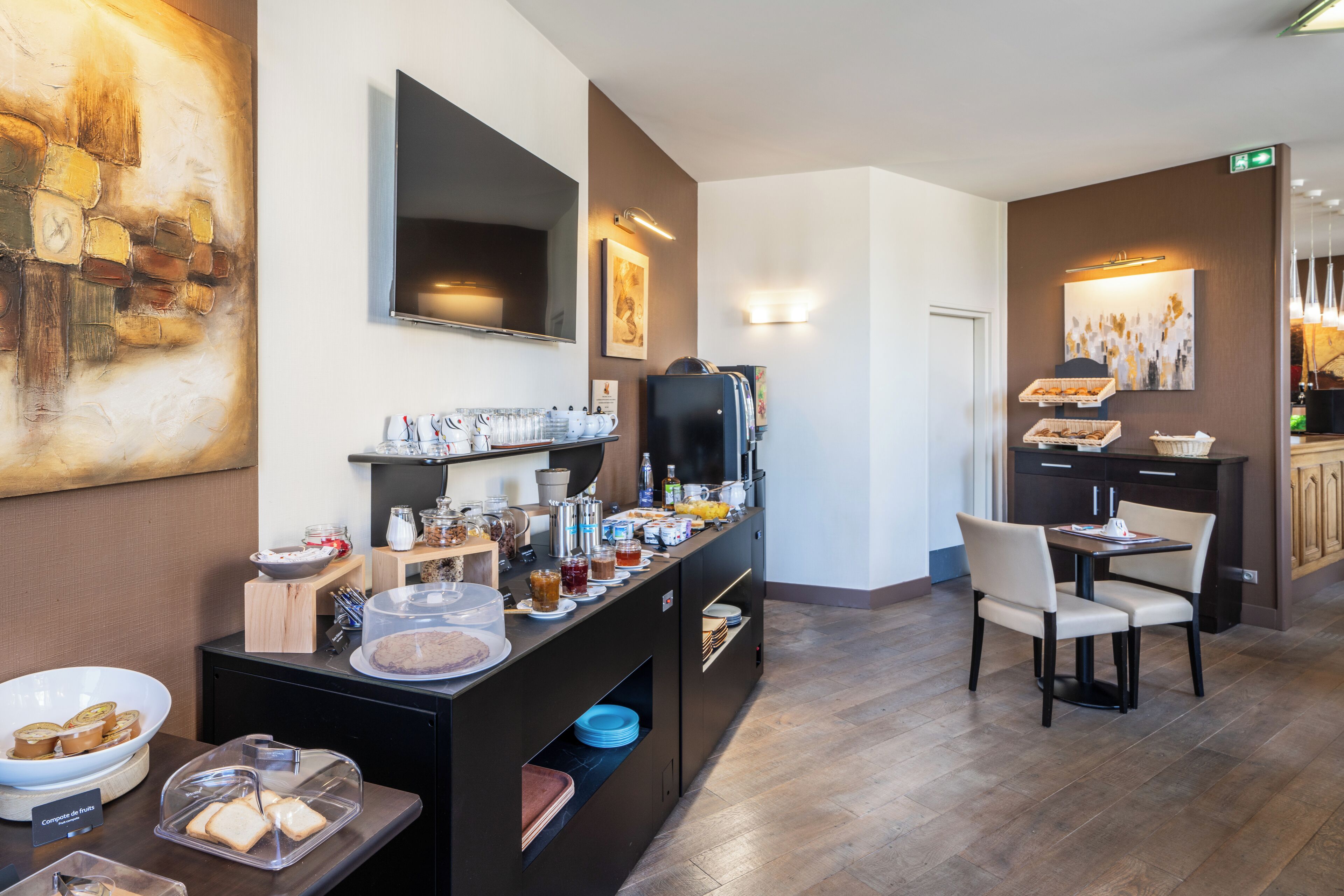 Un comedor de hotel con barra de desayuno, televisor de pantalla plana y obras de arte en las paredes.