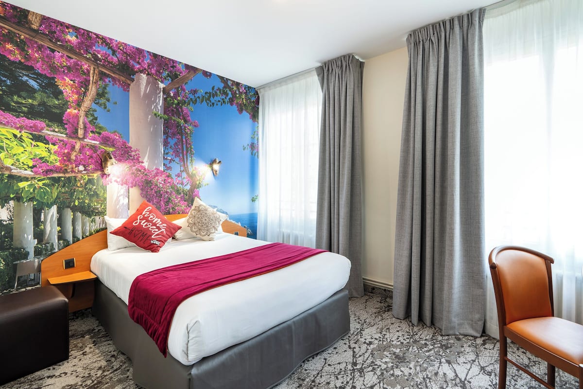 A hotel room with a large bed, a chair, a nightstand, and a wall mural.