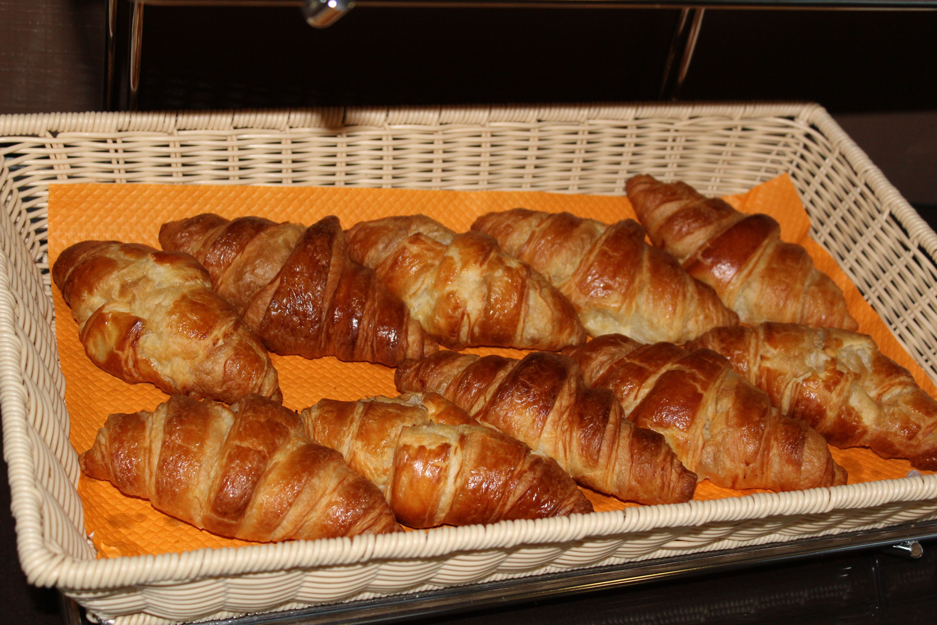 Un panier en osier contenant plusieurs croissants de couleur brun doré, posés sur une feuille de papier orange.