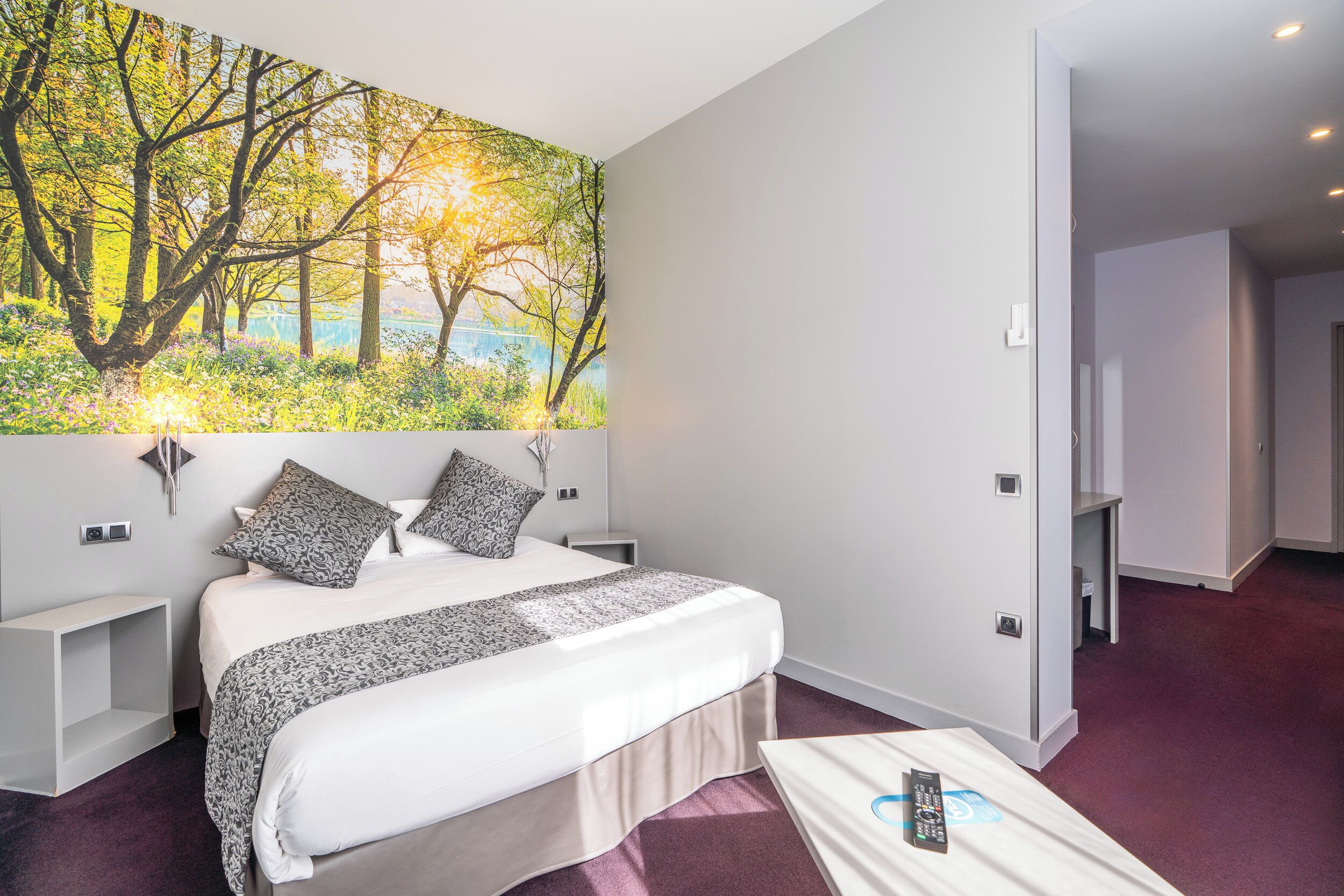 A modern hotel room with a large bed, a nightstand, a bedside table, and a wall-mounted TV.