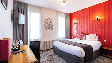 Hotelkamer met een bed, een bureau met een afstandsbediening, een wandtelevisie en een rode accentmuur.