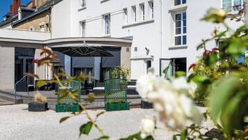 Een hotelentree met een overdekte wachtruimte, buiten zitplaatsen en een grindpad.