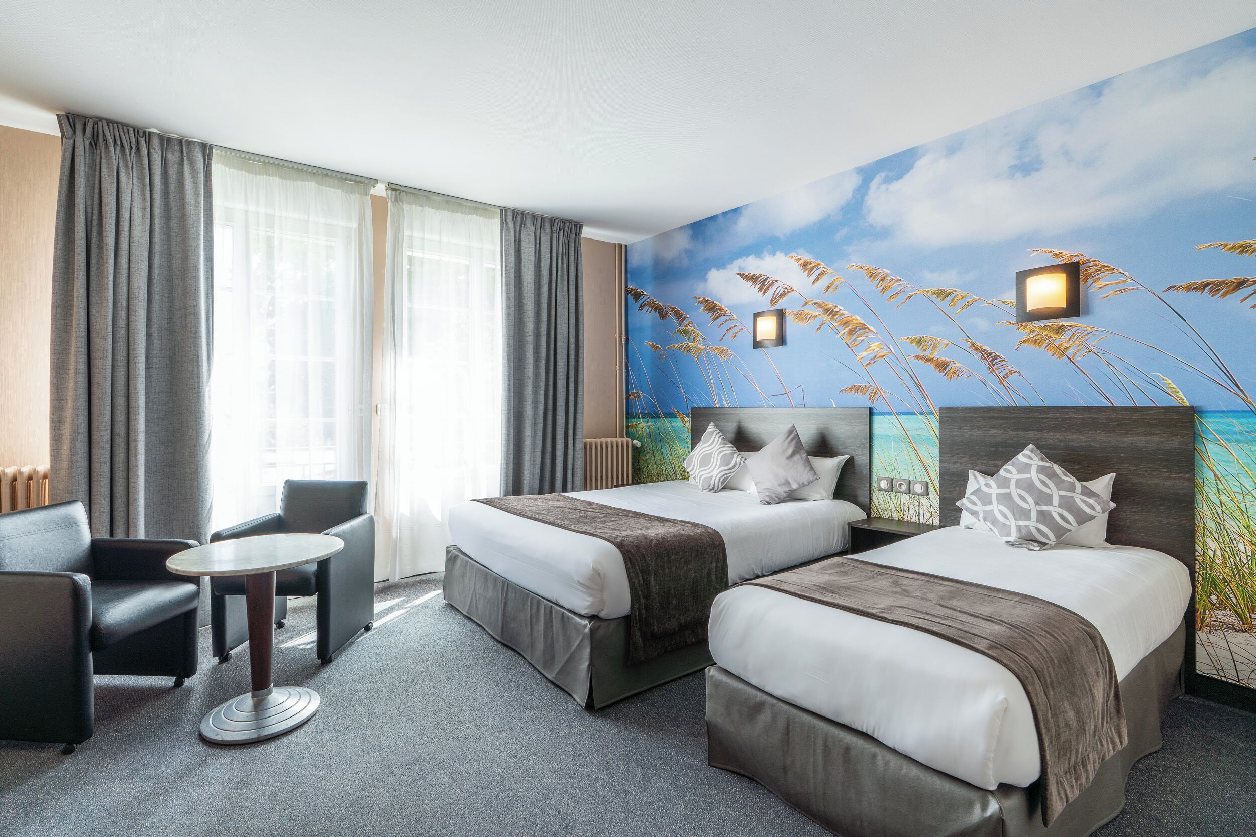 Una habitación de hotel con dos camas, una mesita pequeña y un sofá.