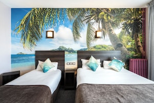 Quarto de hotel com duas camas, um mural de uma praia e palmeiras, e vista para o oceano.