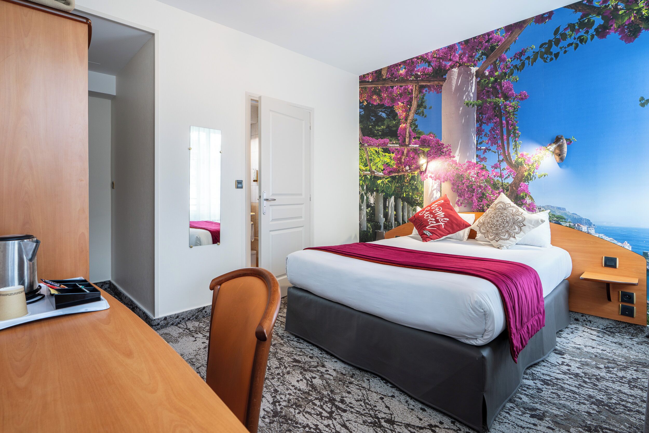 Un dormitorio con una cama grande, un escritorio con hervidor y vista a un paisaje costero por la ventana.