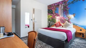 Un dormitorio con una cama grande, un escritorio con hervidor y vista a un paisaje costero por la ventana.