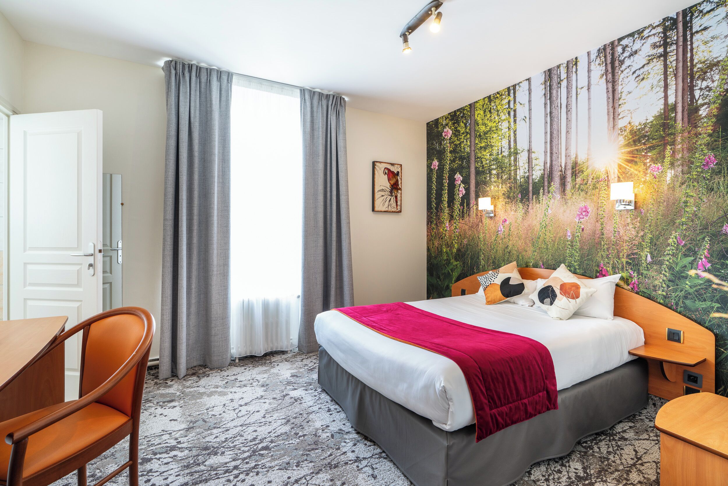 Habitación de hotel con cama, escritorio y silla. Hay un cuadro en la pared y una ventana con cortinas.