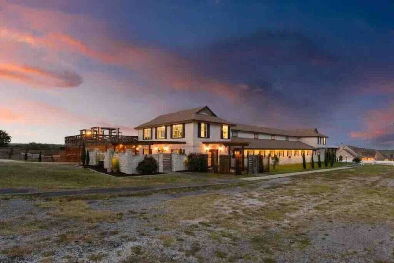 A large, two-story building with a flat roof and multiple windows, surrounded by a gravel driveway and a grassy area.