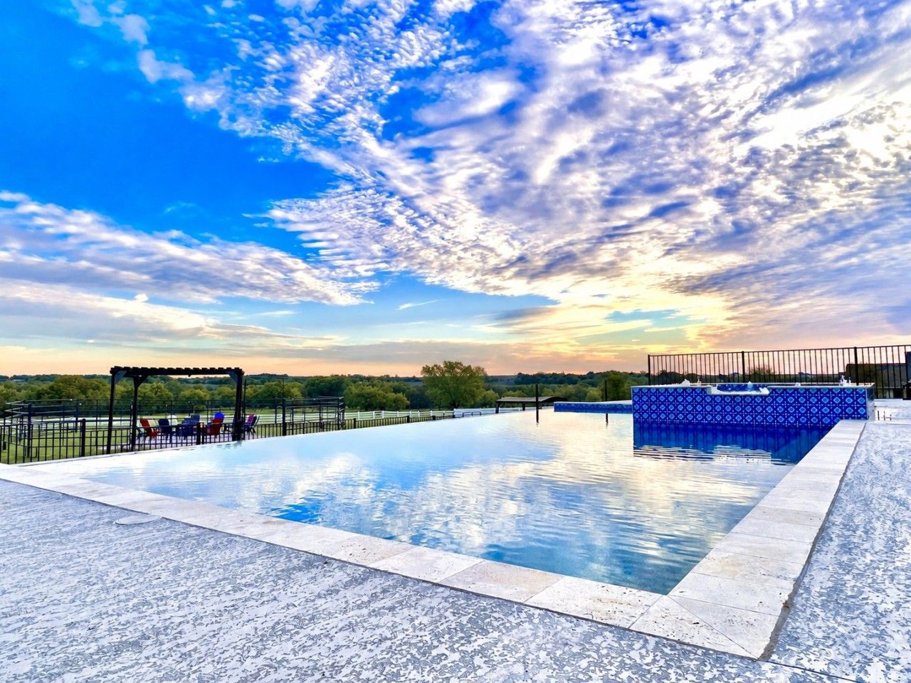 Ein Swimmingpool mit einer Pergola und Liegestühlen, umgeben von einem Zaun.