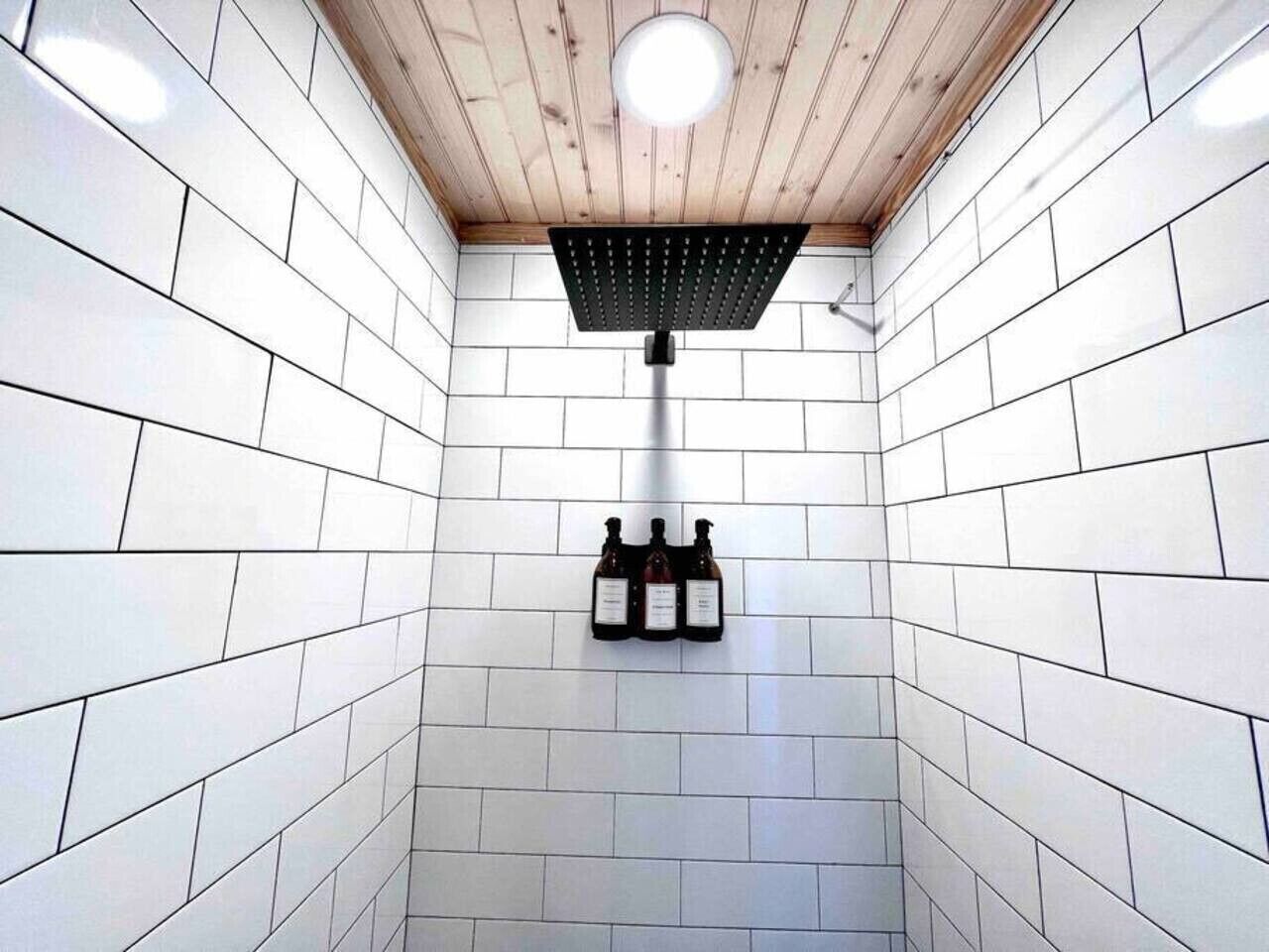 A shower area with white tiles, a wooden ceiling, and a black showerhead.
