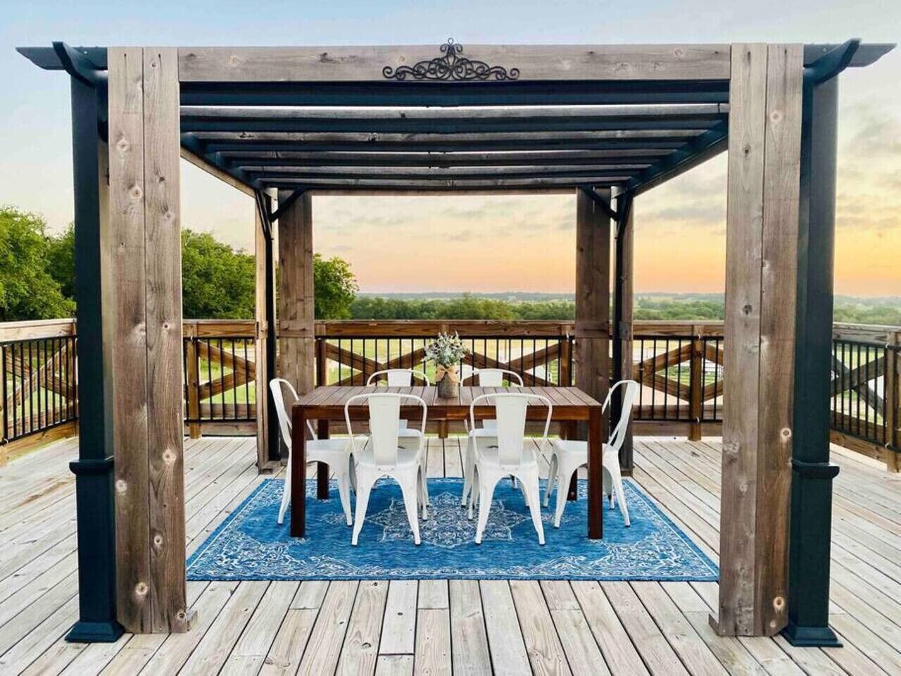 A wooden pergola with a table and chairs on a deck with a view of the landscape.