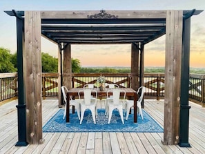 Uma pérgola de madeira com mesa e cadeiras num alpendre com vista para a paisagem.