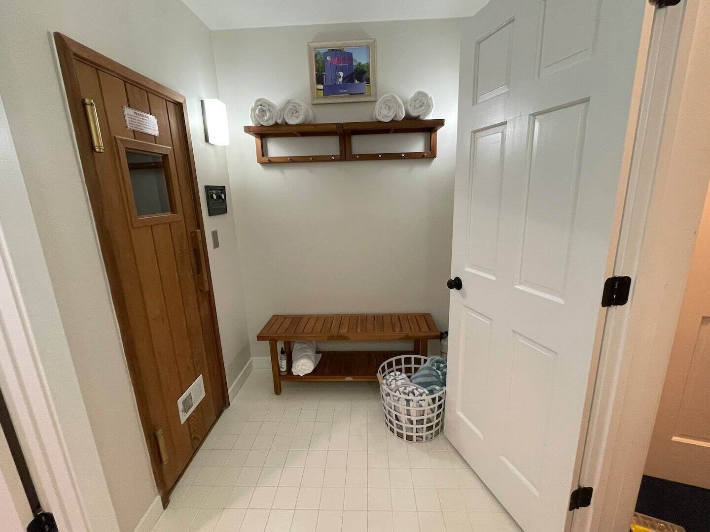 Un couloir avec un banc en bois, une porte blanche et une étagère avec des serviettes.