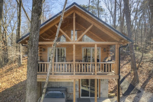 A cabin with a balcony, large windows, and a stone foundation.