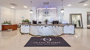 Un mostrador de recepción en Ocean Reserve con encimera de mármol, dos lámparas colgantes y un felpudo negro.