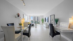 Una habitación de hotel moderna con zona de comedor, un amplio ventanal con vista a la ciudad y un cartel que dice "Sparkle".